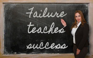 woman standing in front of blackboard pointing to handwritten words in chalk "Failure teaches success"